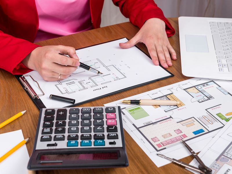 A calculator, pencils and printed floor plans on a desk while a person marks up a plan.