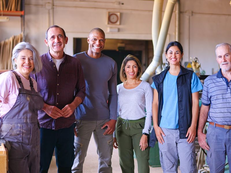 A diverse group of six smiling coworkers standing together in a workshop.